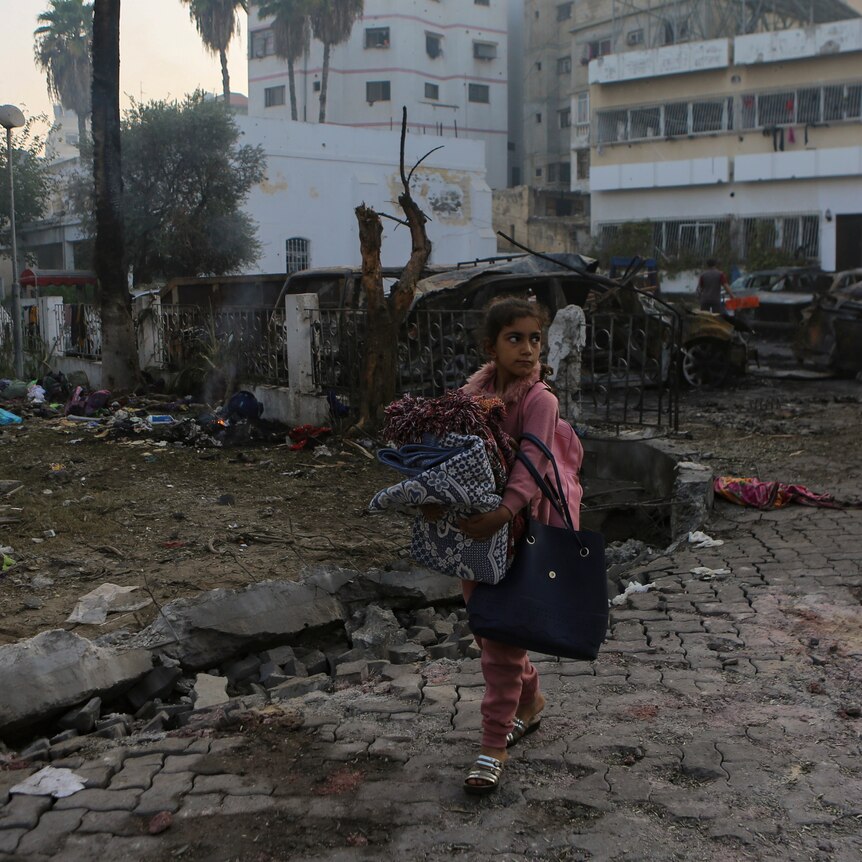 A gir walks through an area with destruction shown behind her.