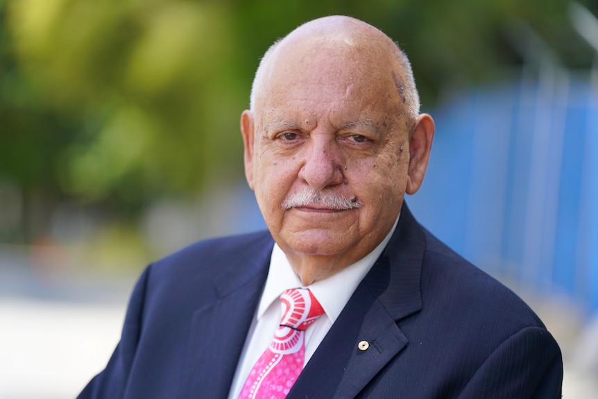 A distinguished older gentleman looks at the camera, he has a moustache and wears a suit and tie