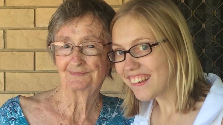 An elderly woman in a green top poses for a photo with a young woman with blonde hair