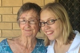 An elderly woman in a green top poses for a photo with a young woman with blonde hair