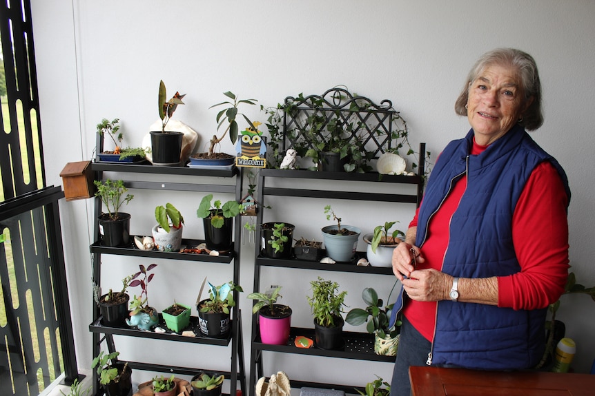 An elderly woman standing in front of shelves full of potplants.