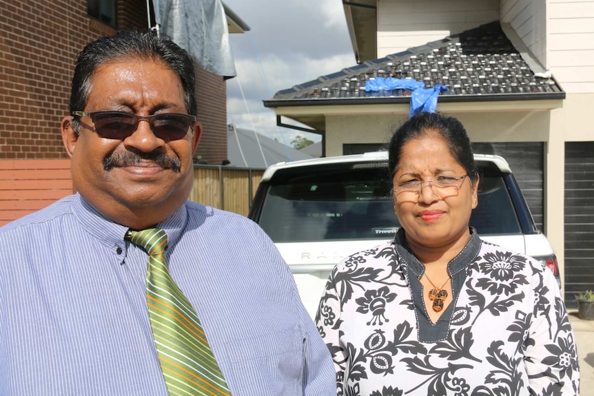 A husband and wife standing in front of their house.