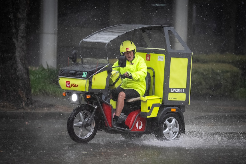 A postie in high vis gear drives a delivery tricycle.