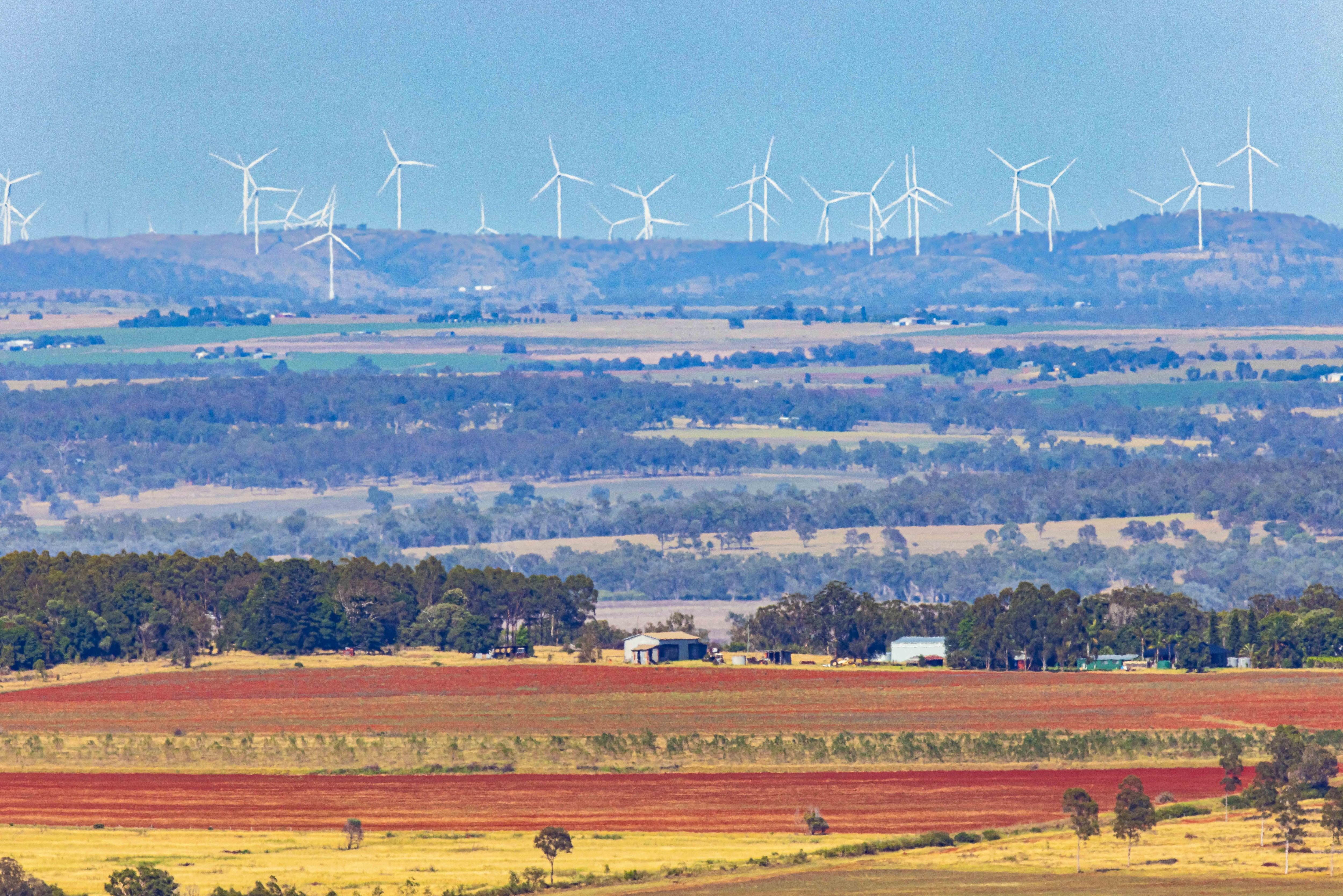 A photo of farmlands with a wind farm in the background. 