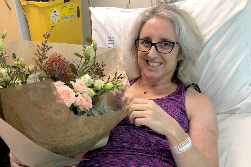 Justine Barwick on her hospital bed holding a bunch of flowers and smiling.
