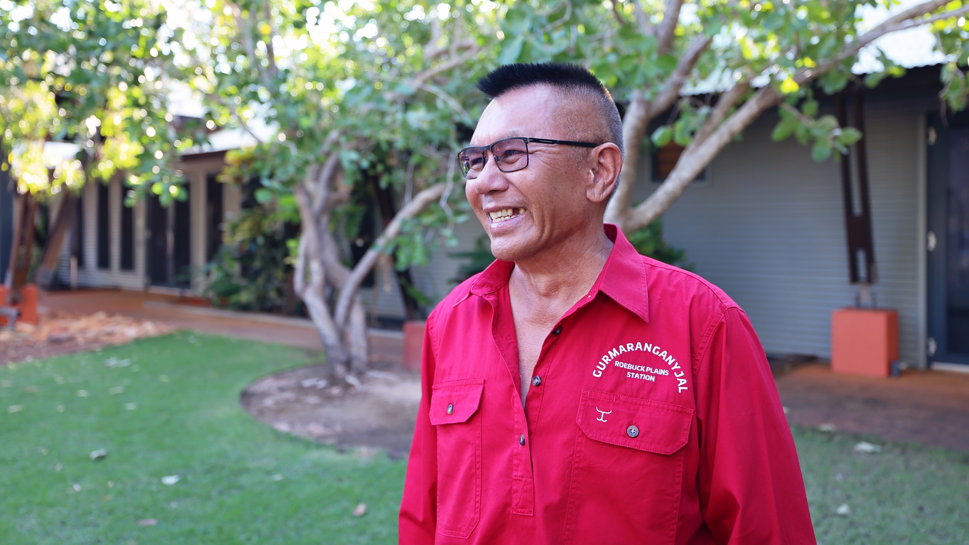 A man in a red shirt looks away from the camera smiling
