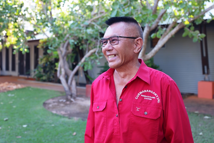 A man in a red shirt looks away from the camera smiling