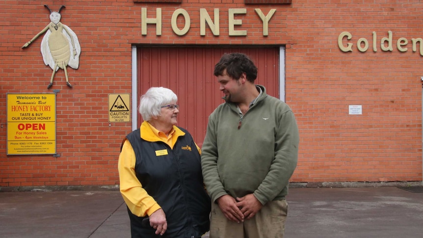 An older woman and a younger man stand outside a brick building smiling at eachother.