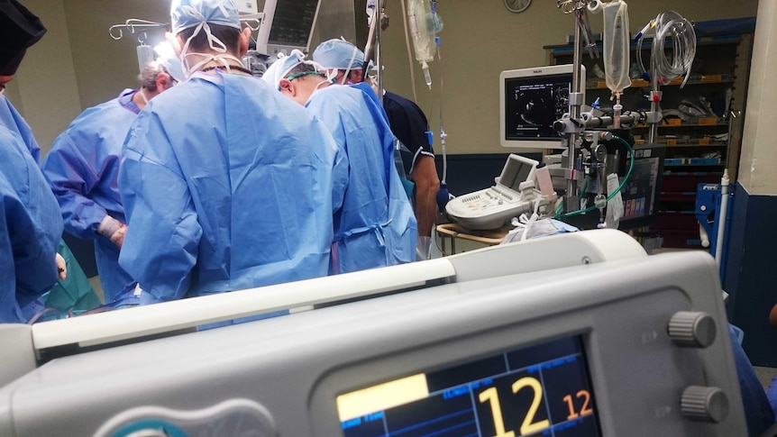 A group of doctors pictured during a surgical operation, with a heart rate monitor in the foreground.