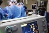 A group of doctors pictured during a surgical operation, with a heart rate monitor in the foreground.