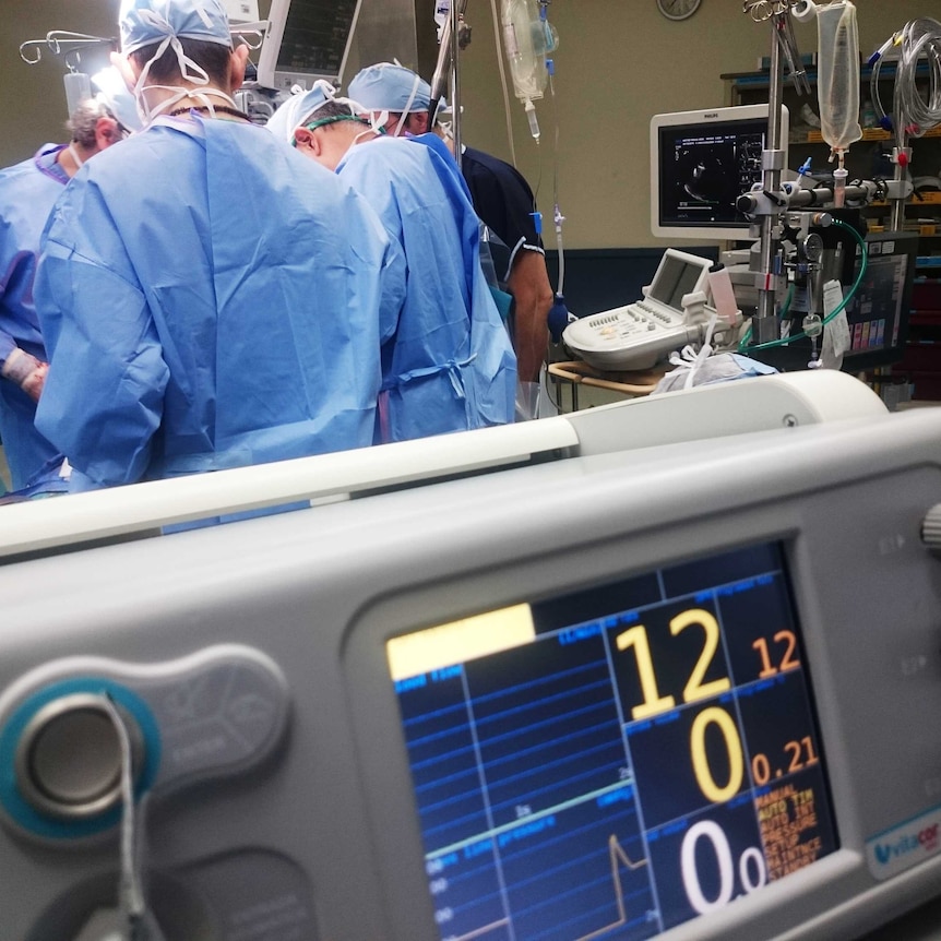 A group of doctors pictured during a surgical operation, with a heart rate monitor in the foreground.