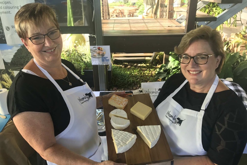Sandra Cadby and Karen Paynter hold up a platter of cheese, smiling at the camera.