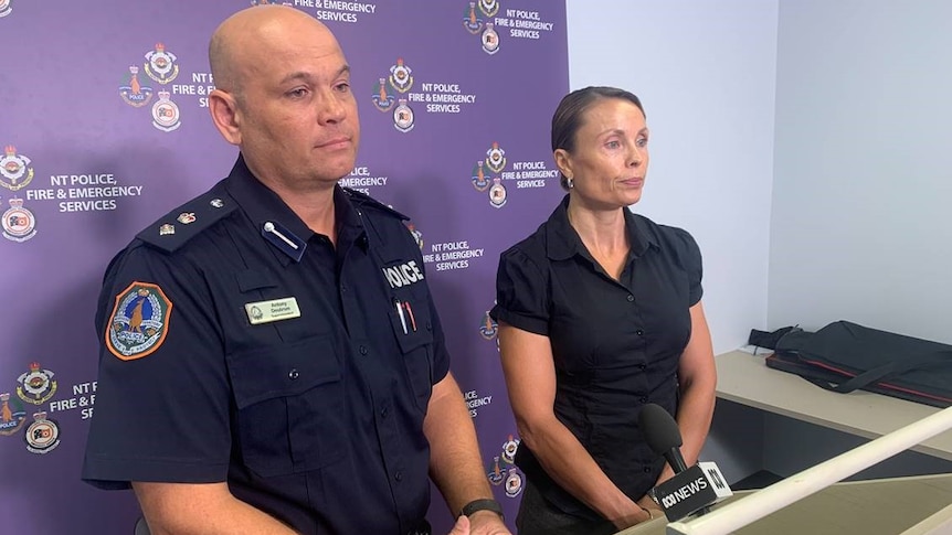 Bald man standing in dark blue police uniform and a woman to the right wearing all black.