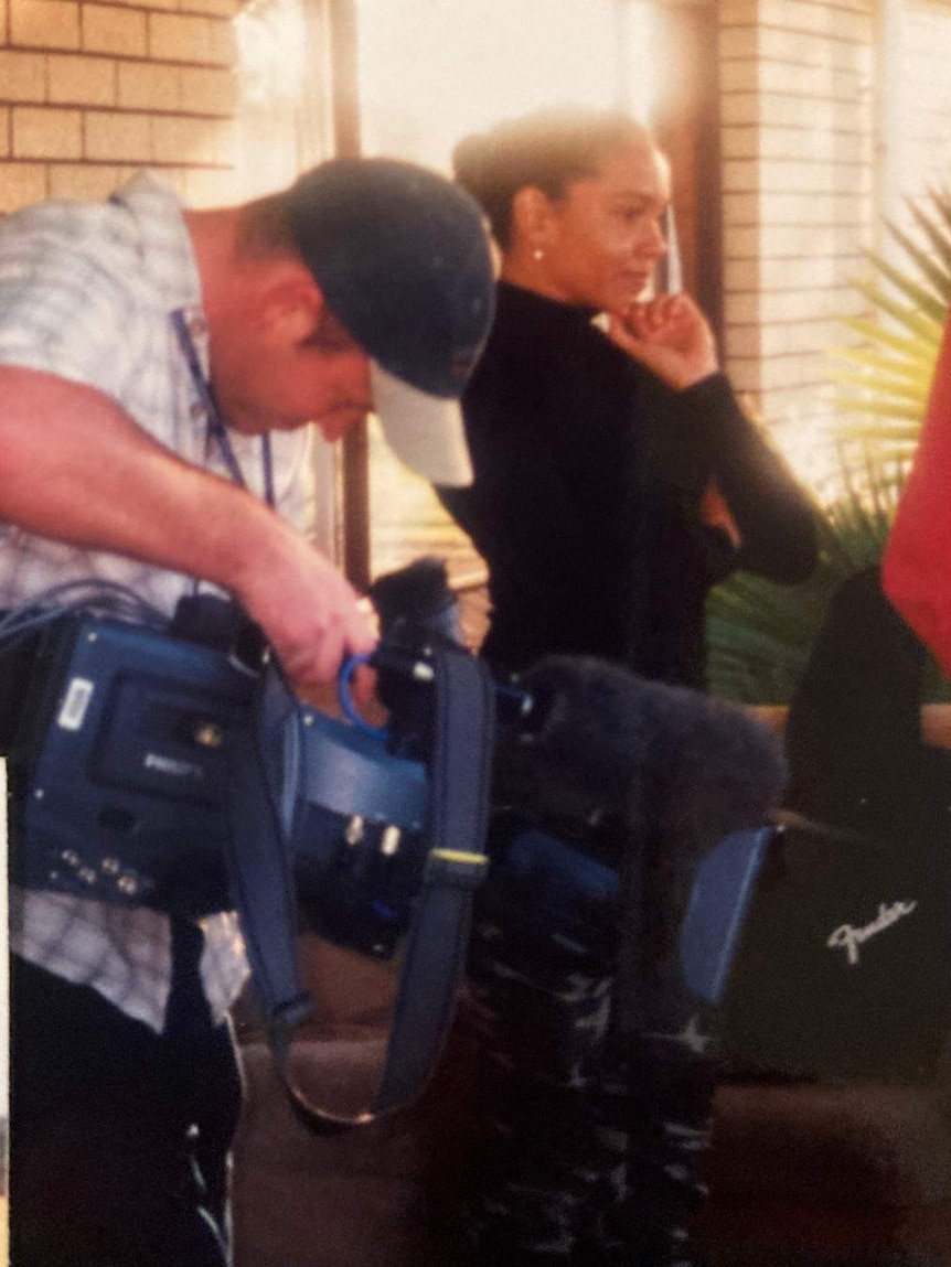 Corowa standing next to cameraman looking into viewfinder of his camera.