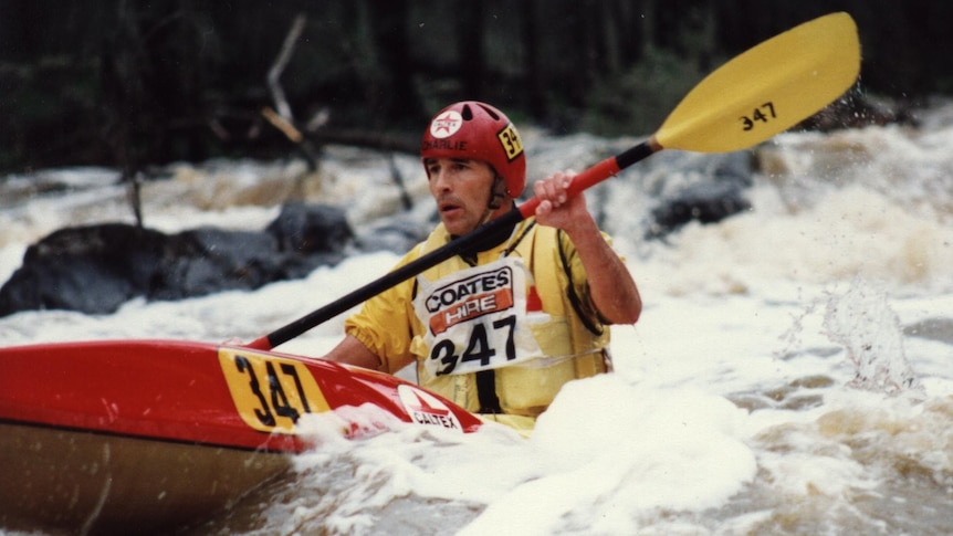 A man in a red kayak, traversing the whitewater rapids, wears red helmet, yellow jersey with 347 number.