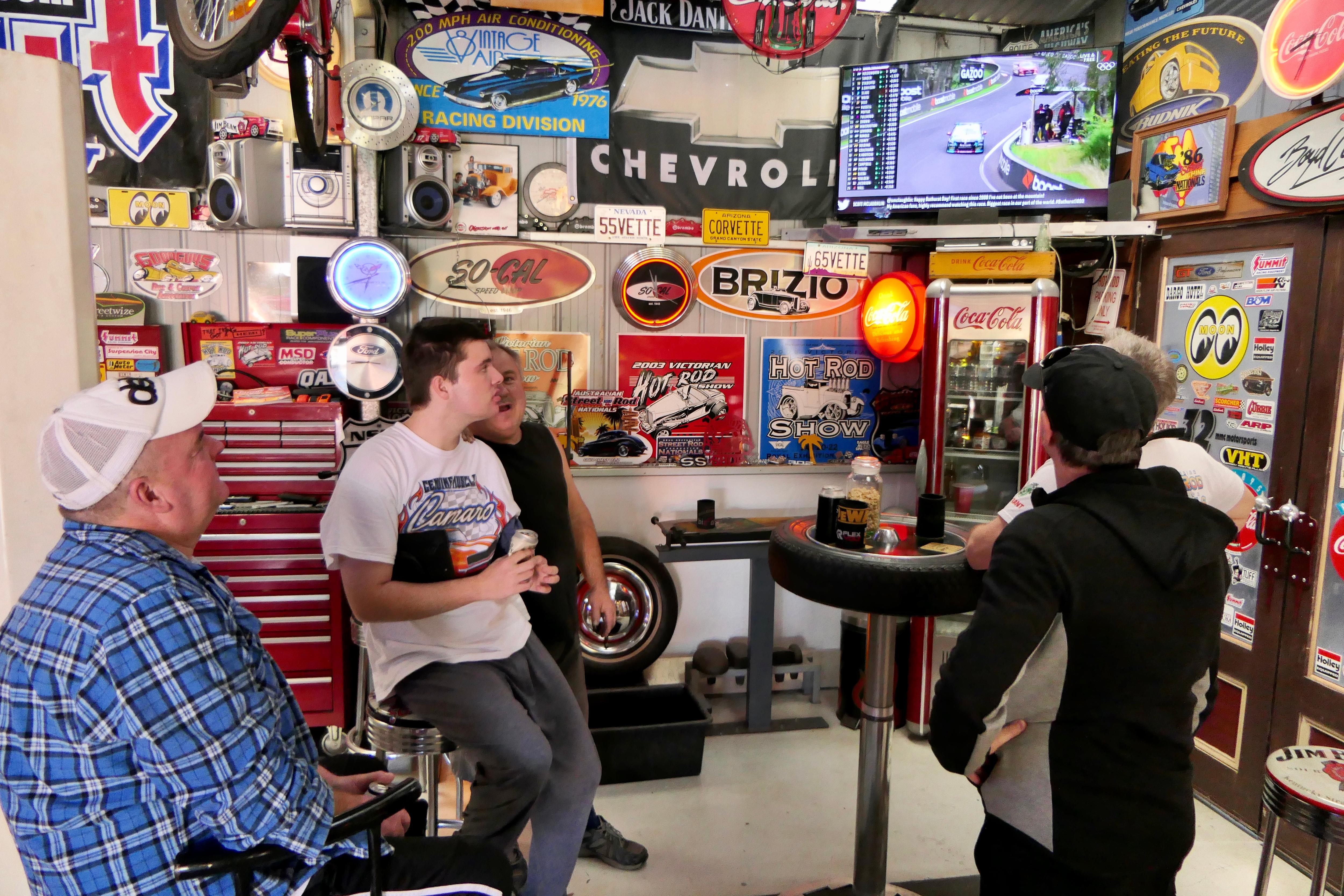 Group of men look up at TV screen showing car race.