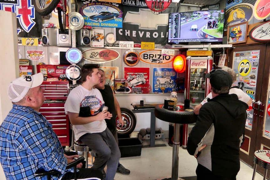 Group of men look up at TV screen showing car race.