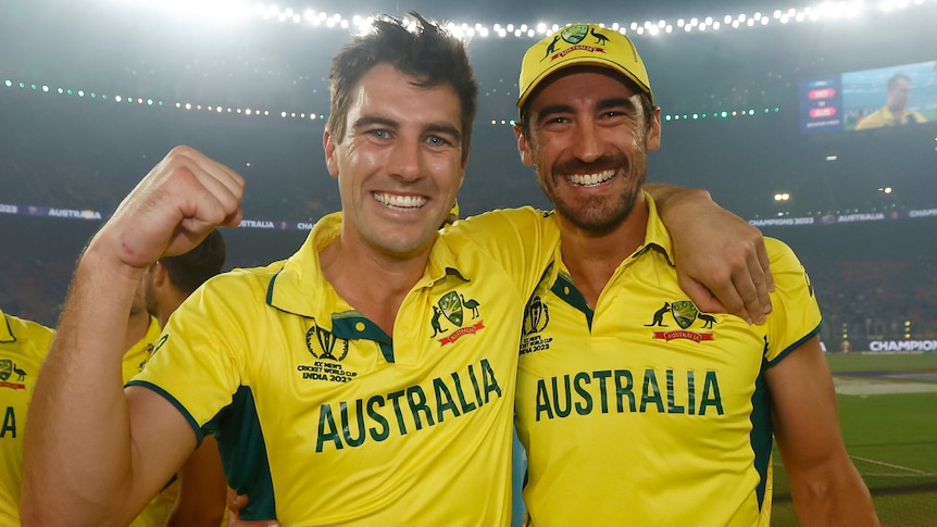 Two male cricket players in Australia kit embrace and celebrate.