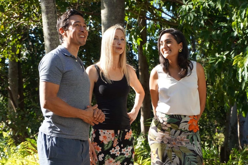 A couple stand with Del in front of vibrant green foliage