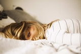 Woman lying face down on bed with her hair obstructing her face and looking tired to depict sleep problems.