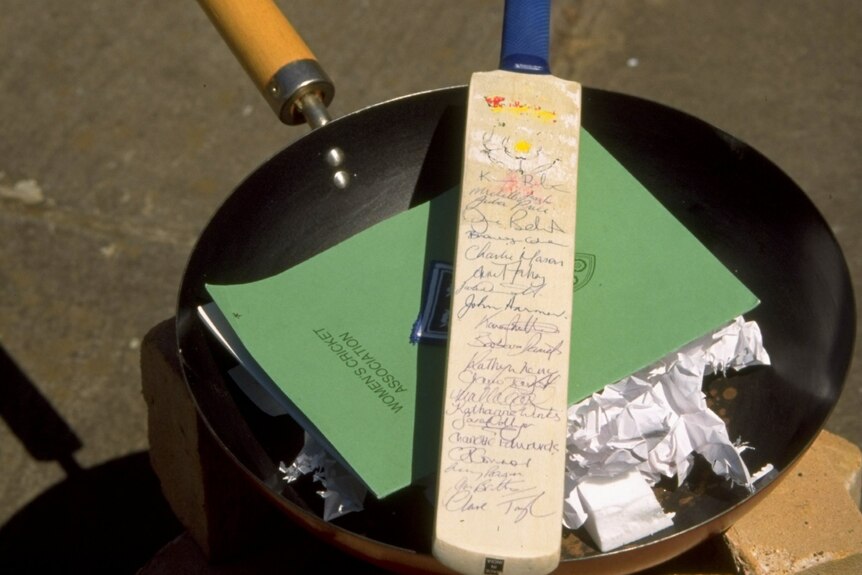A bat sits on top of papers and a wok, ready to be burnt.