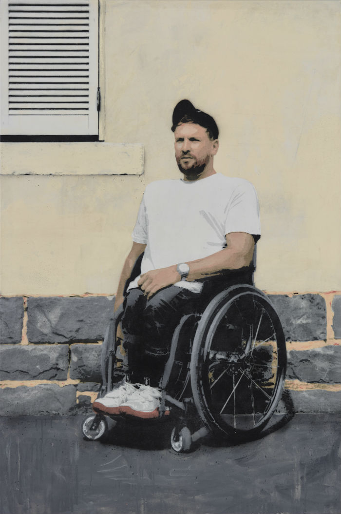 Alcott in a white t-shirt, black jeans and a black cap is rendered in a graffiti style against a brick and rendered wall.