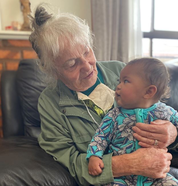 woman with gray hair, looking down at a baby, sit in a black chair. 