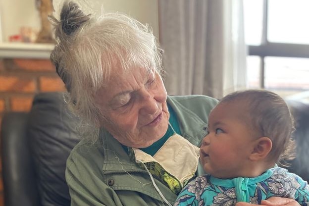 woman with gray hair, looking down at a baby, sit in a black chair. 