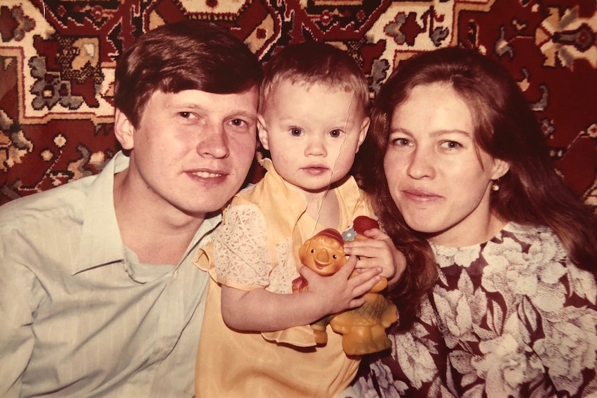 Old photo of a young man and woman holding a baby girl in a yellow dress in between them.