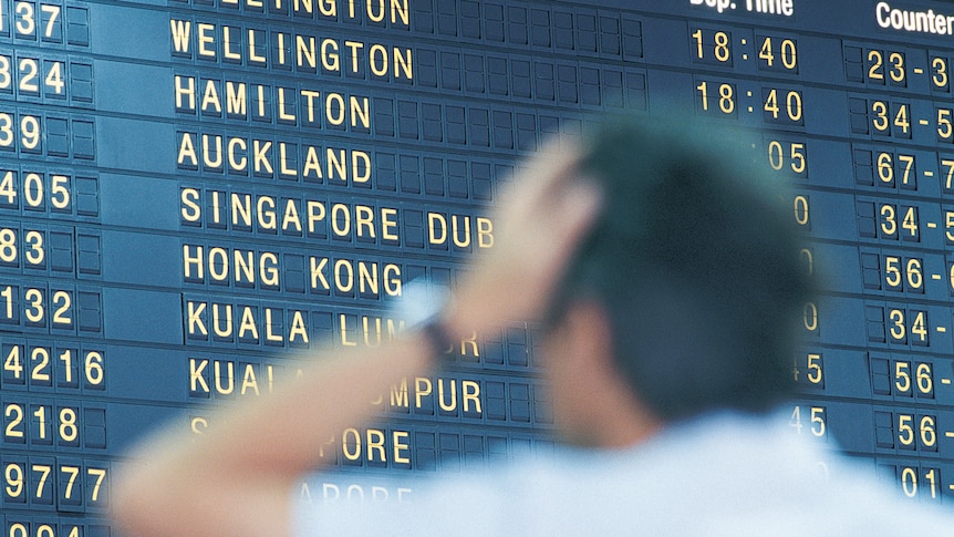 A man looking confused looking at the airport departures board