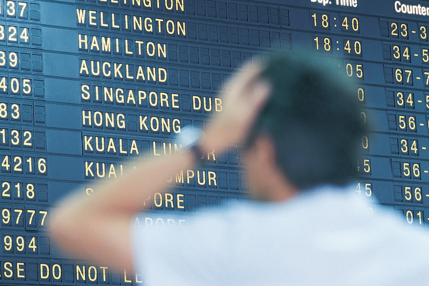 A man looking confused looking at the airport departures board