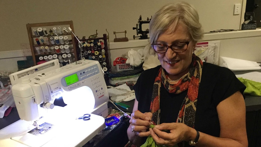 A woman does some hand sewing near a sewing machine.