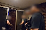 the blurred figures of four police officers as they prepare to enter a residence.