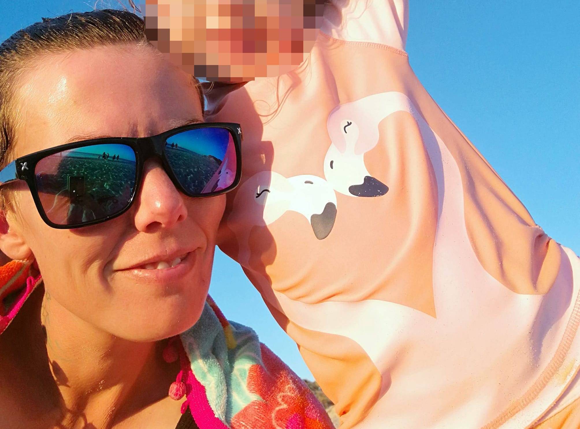 A mother wearing sunglasses holds a child.