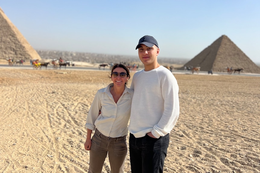 A woman stands next to a man with pyramids behind them.