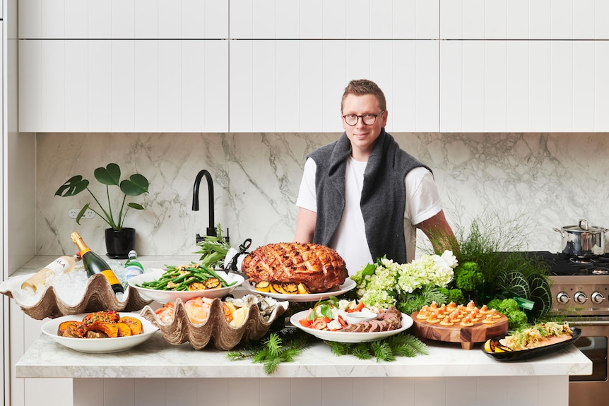 Alex Cadger stands behind a kitchen bench covered in Christmas foods.
