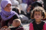 Yazidi woman sits with children after fleeing IS advances.