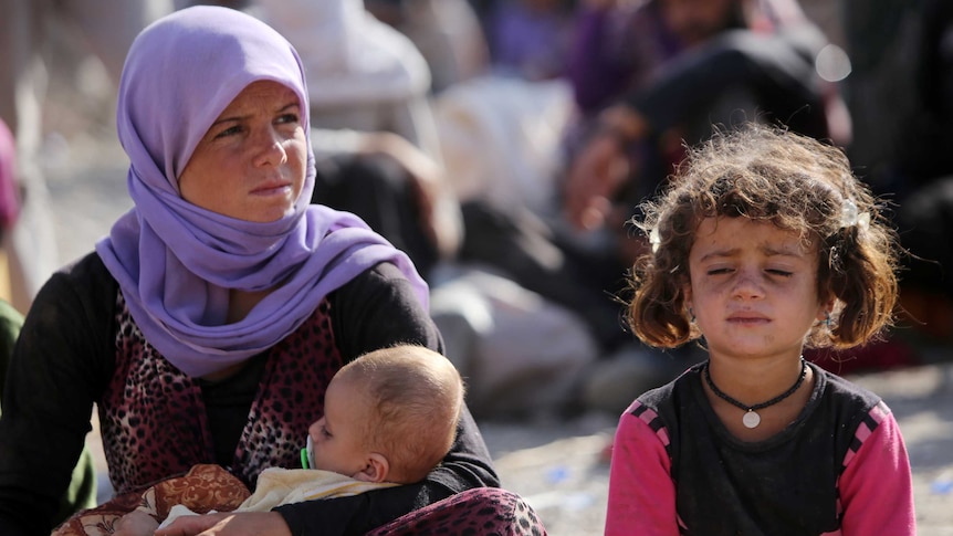 Yazidi woman sits with children after fleeing IS advances.