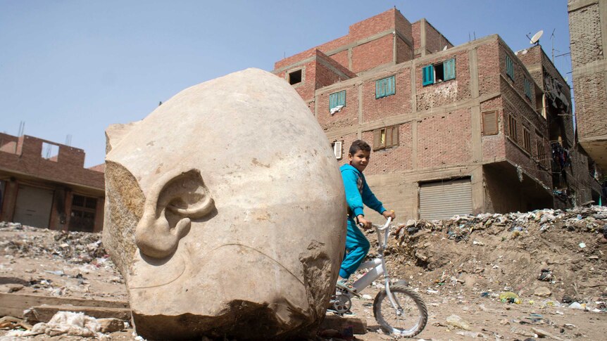 A boy rides his his bicycle past a recently discovered statue in a Cairo slum that may be of pharaoh Ramses II