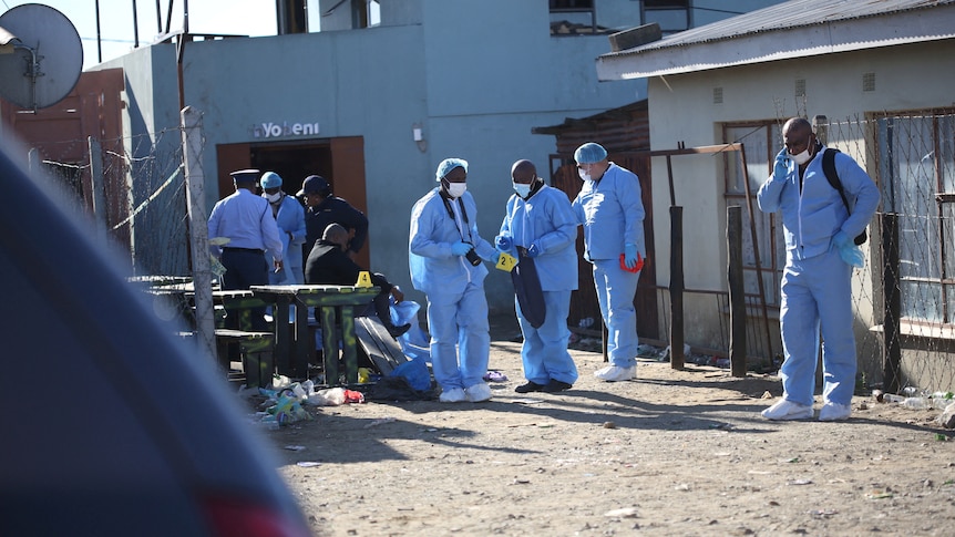 Forensic personnel in blue coveralls outside a club.