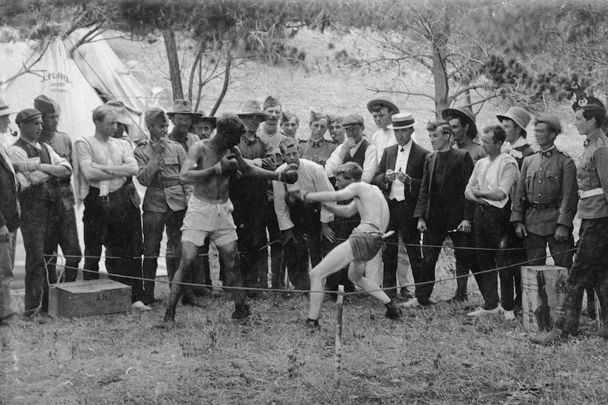 A boxing match in a bush setting in 1909, with a tent with 'J. Flavel' stencilled on it in the background.