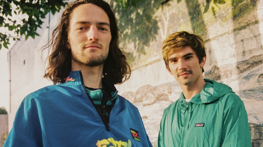 The two members of Close Counters stand in an alleyway wearing bright tracksuit tops, smiling at the camera