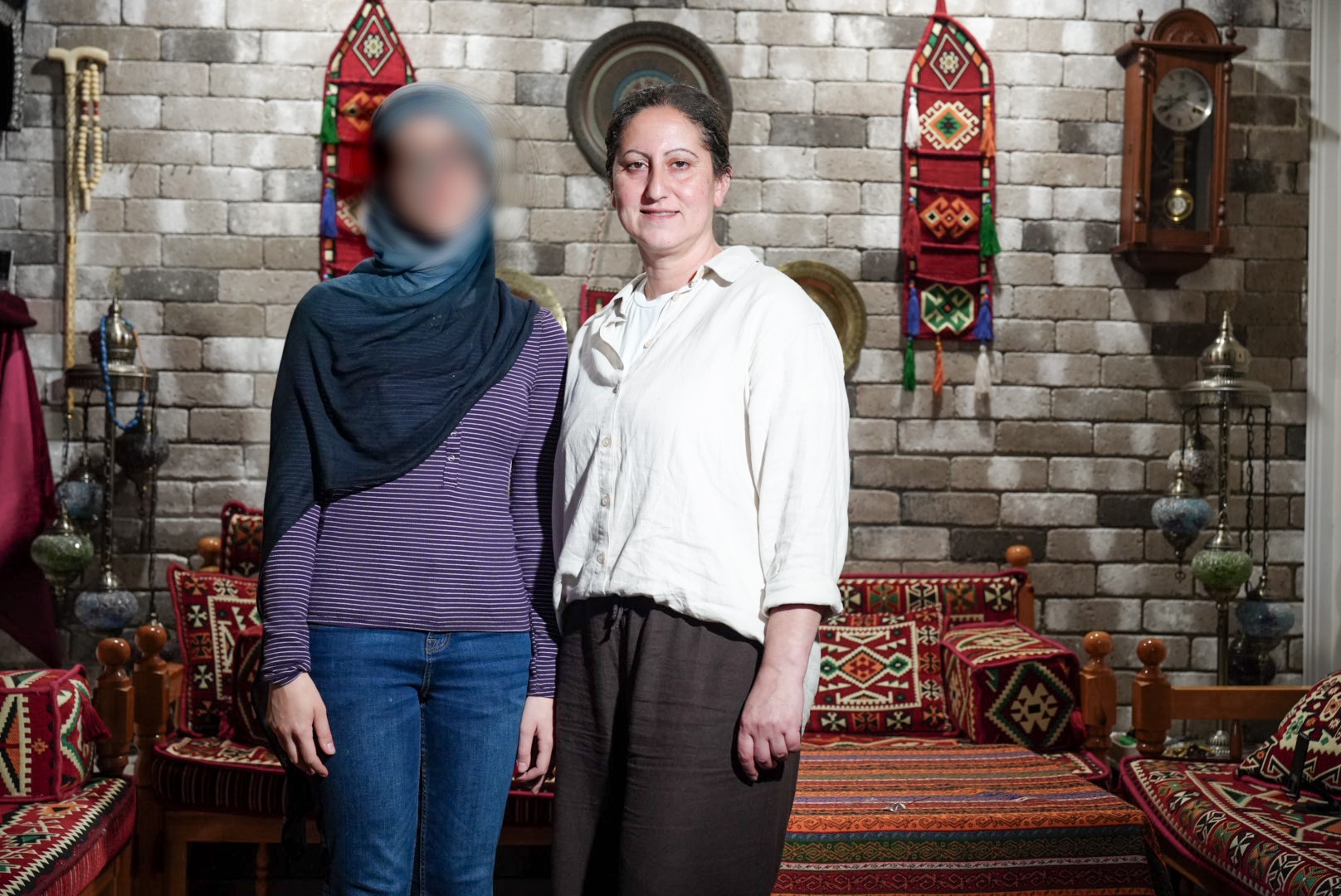 Janna is a petite teenager, her face is blurred. She is next to mum Roula. Behind them are bright textiles.