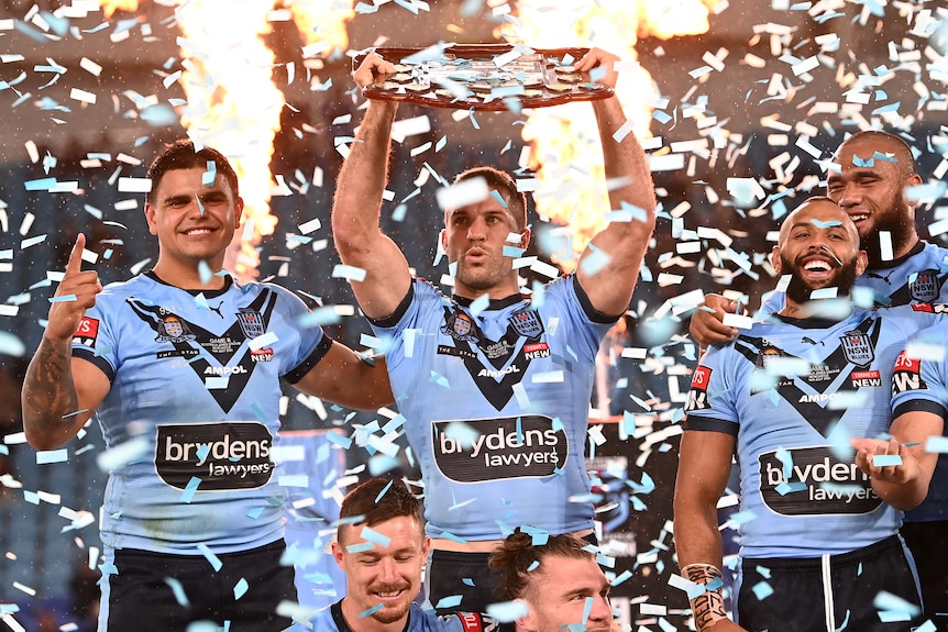 James Tedesco lifts the State of Origin shield as confetti falls. Latrell Mitchell and Josh Addo-Carr are next to him.