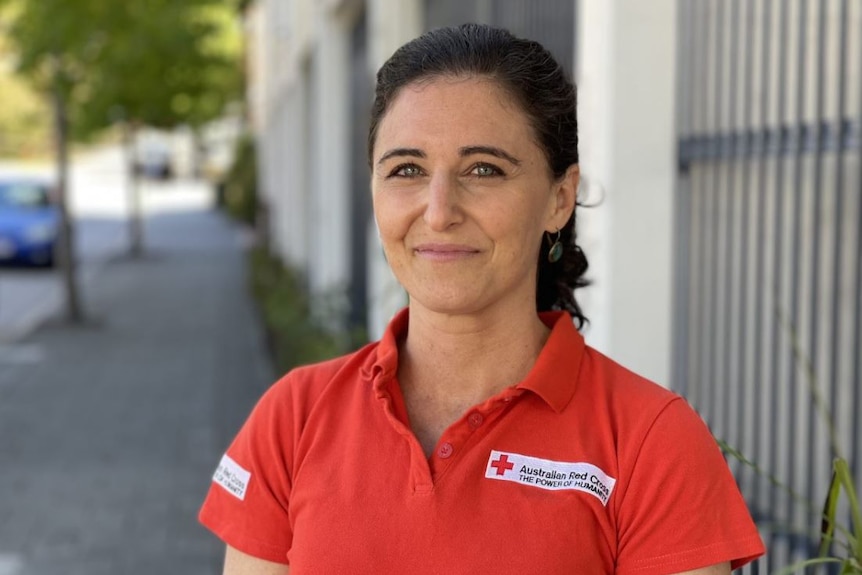 Liza Beinart wears a bright red shirt and smiles standing on a street