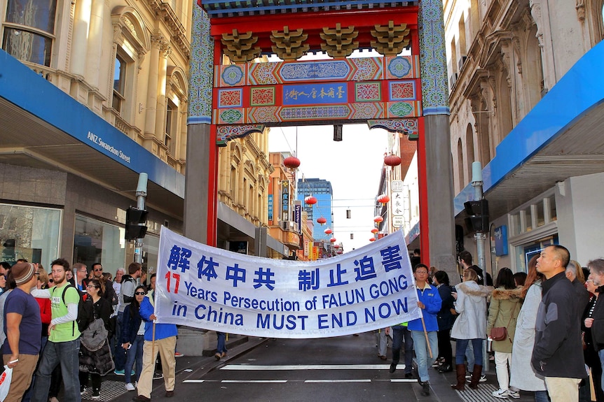 Falun Gong practitioners marching in Melbourne Chinatown with crowd looking at them from both sides.