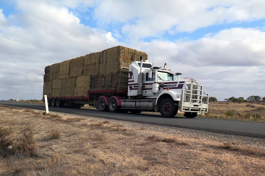 A truck on a country road with a load of hay on the trailer.
