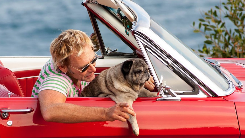 Damien and dog in a red convertible.