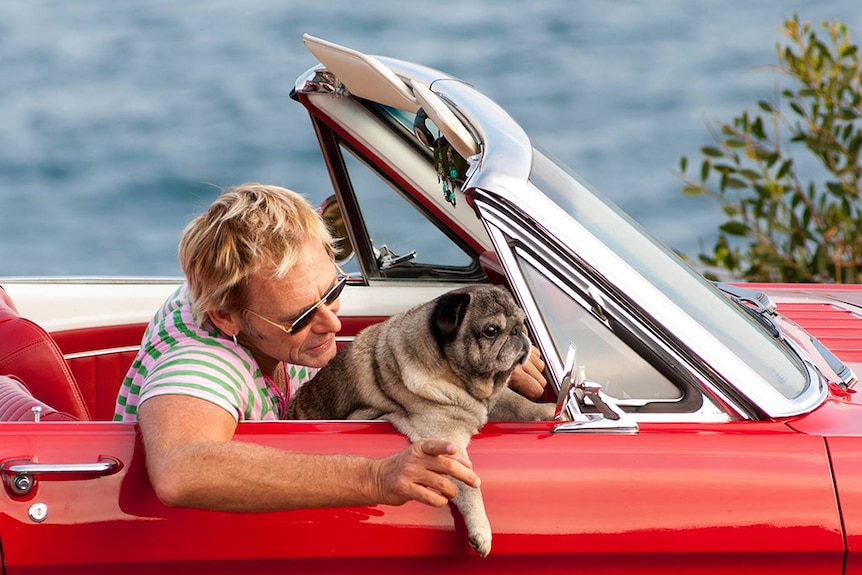 Damien and dog in a red convertible.