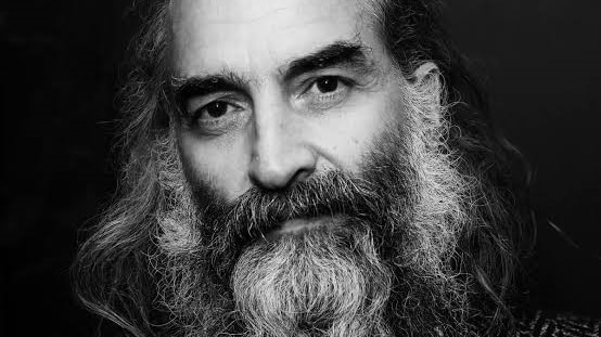 Black and white head shot of musician Warren Ellis looking straight at the camera.  He has a long greying beard.